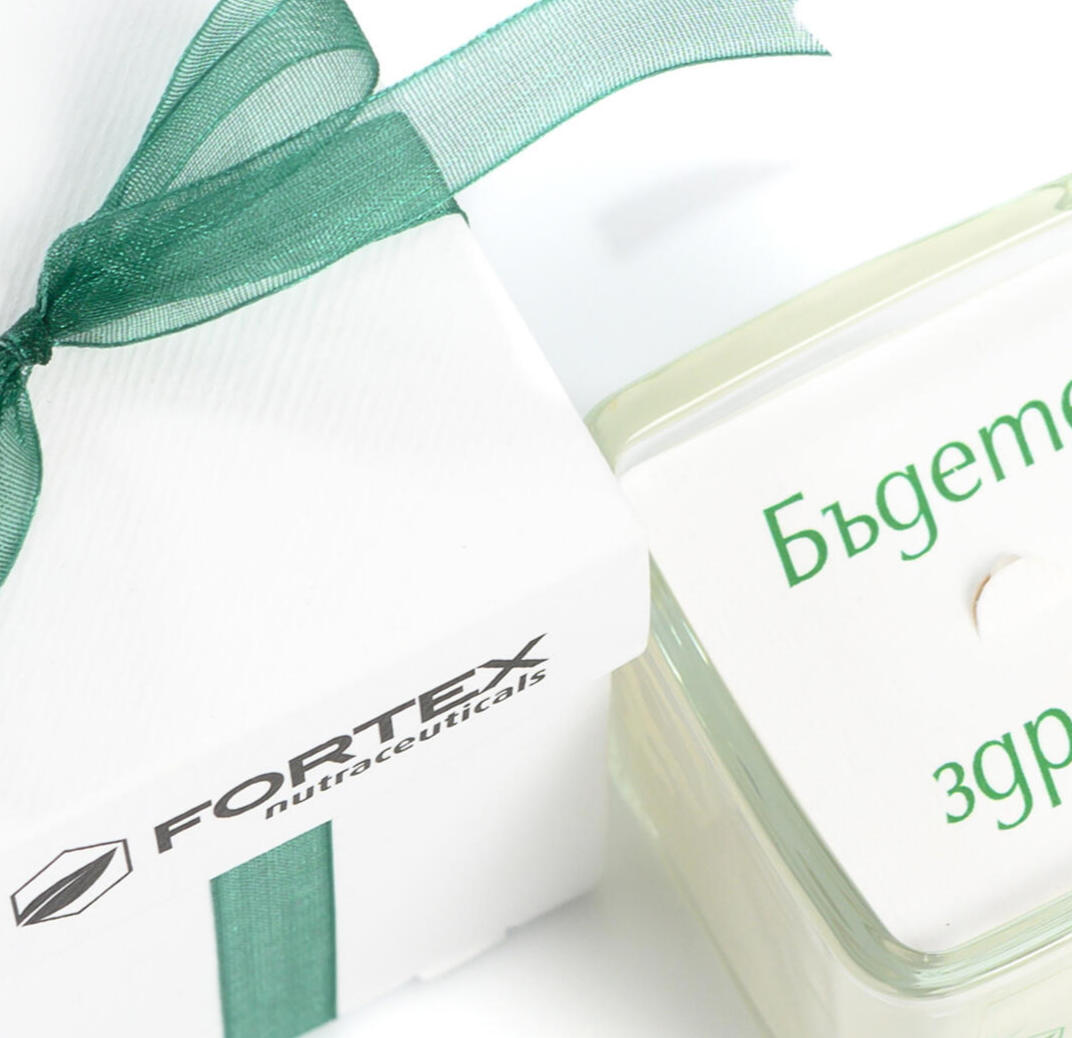 Реален детайл от FORTEX: бяла подаръчна кутия, зелена панделка и свещ с послание „Бъдете здрави!“.